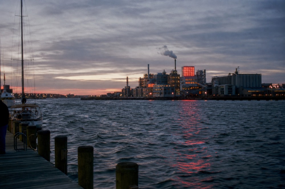 The Domino Sugars neon sign glowing red at dusk above the Locust Point refinery, its reflection stretched across the dark Patapsco River