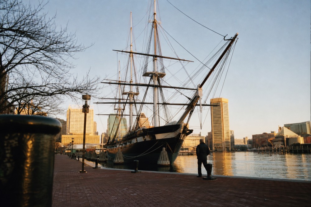 The USS Constellation's tall masts and rigging against a clear sky at Pier 1, the historic sloop-of-war moored along the brick promenade