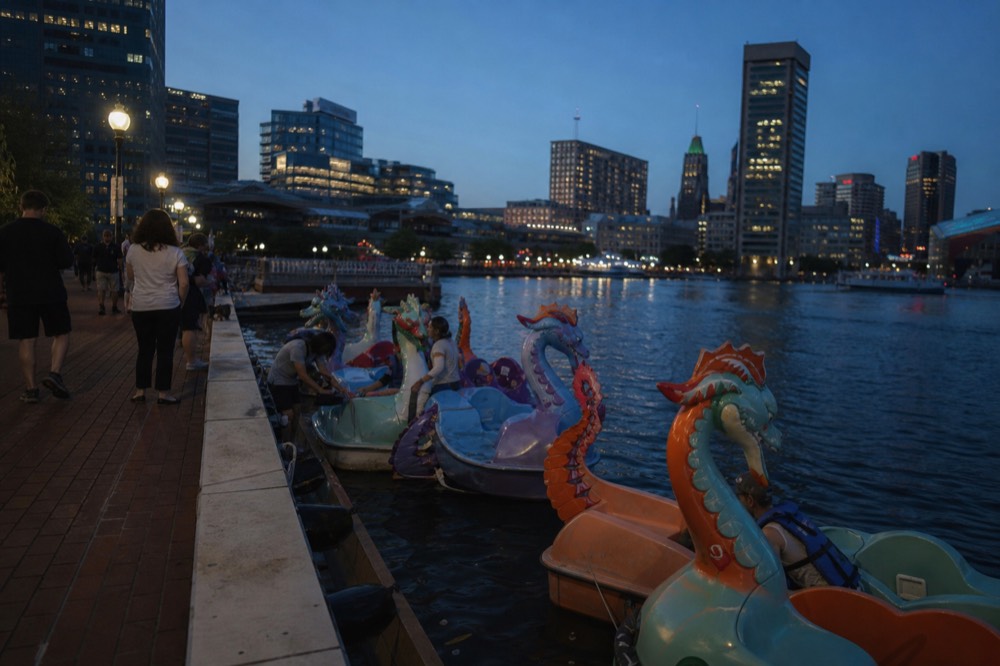Colorful pedal paddle boats shaped like dragons clustered near the promenade in the Inner Harbor basin, families climbing aboard under a clear summer sky