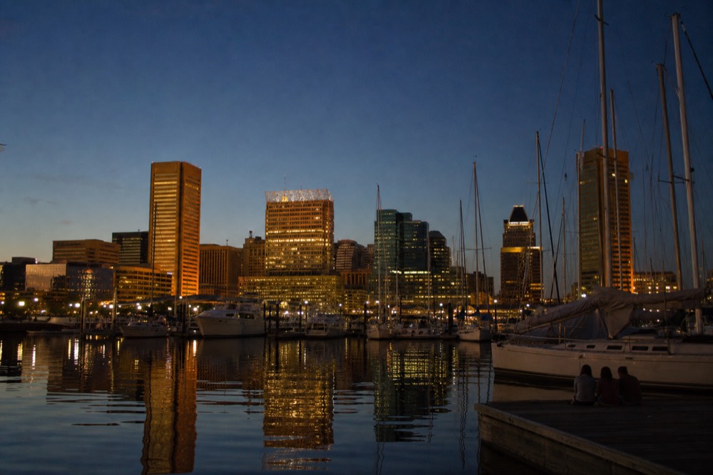 The downtown skyline seen from the water just after sunset, office towers lit warm gold against a deep indigo sky, the harbor calm and mirror-still below
