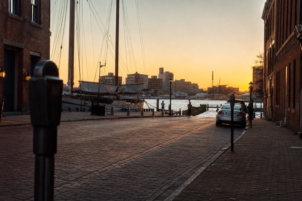A metered parking spot on a brick-paved downtown street near the harbor, a payment pole in the foreground and the water visible at the end of the block