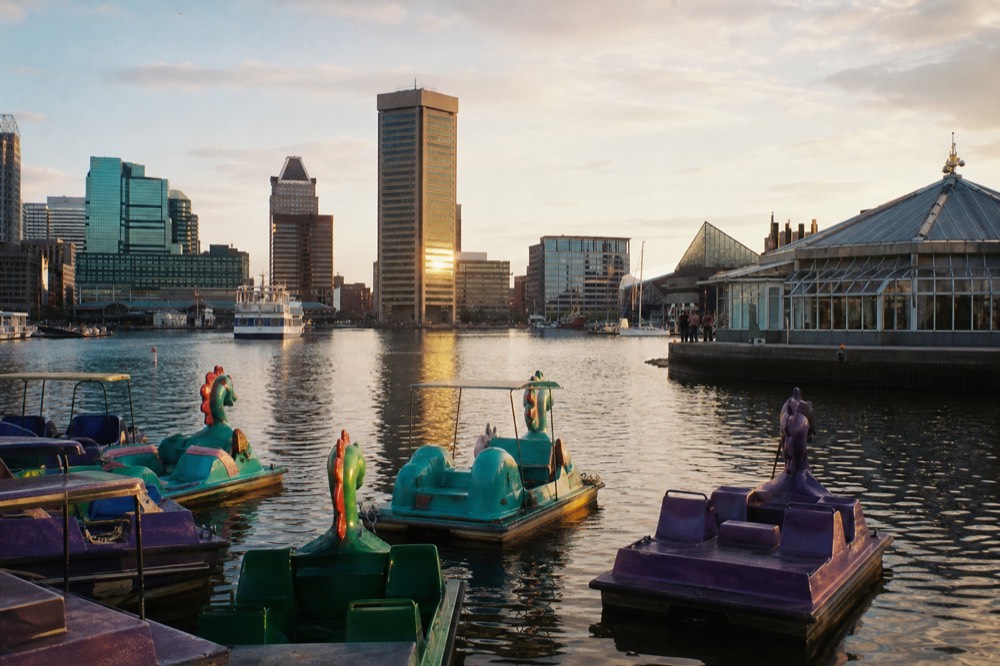 Brightly colored paddleboats clustered on the calm harbor near a glass-domed pavilion, the downtown skyline behind them under a warm afternoon sky